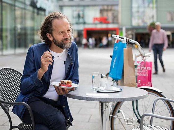 Mann sitzt an einem Kaffeehaustisch im Freien, an einer Fußgängerzone in der Linzer Innenstadt.