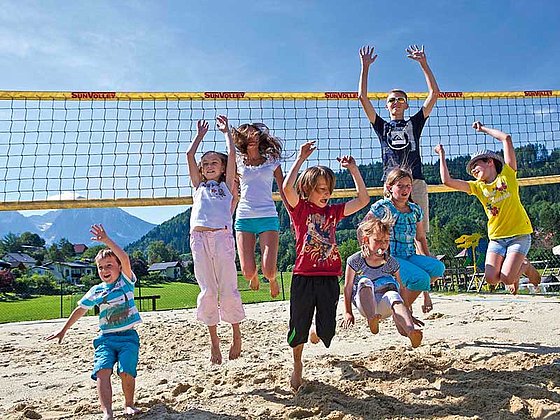 einige Kinder springen im Sand am Volleyballplatz
