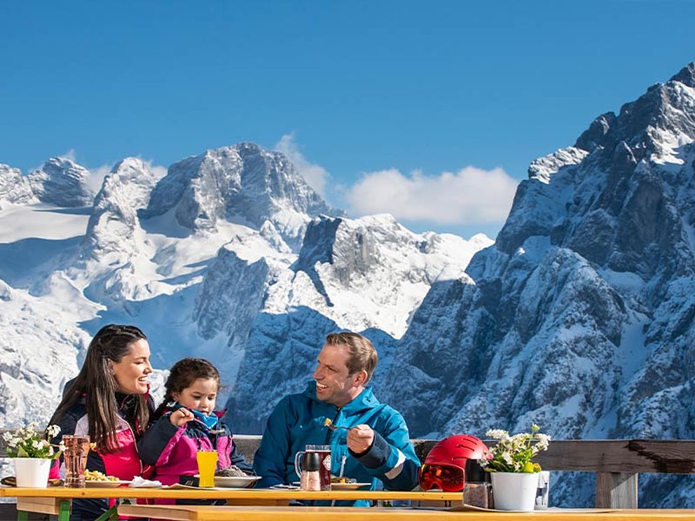 Eine Familie beim Mittagessen, im Hintergrund der Dachstein