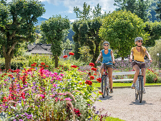 zwei Radfahrerinnen radeln durch die schönen Gärten in Bad Ischl im Salzkammergut