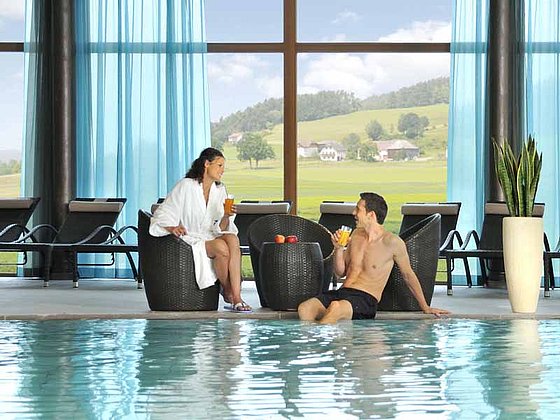 Ein Paar am Beckenrand am Indoor Pool im Hotel Falkensteiner, Bad Leonfelden
