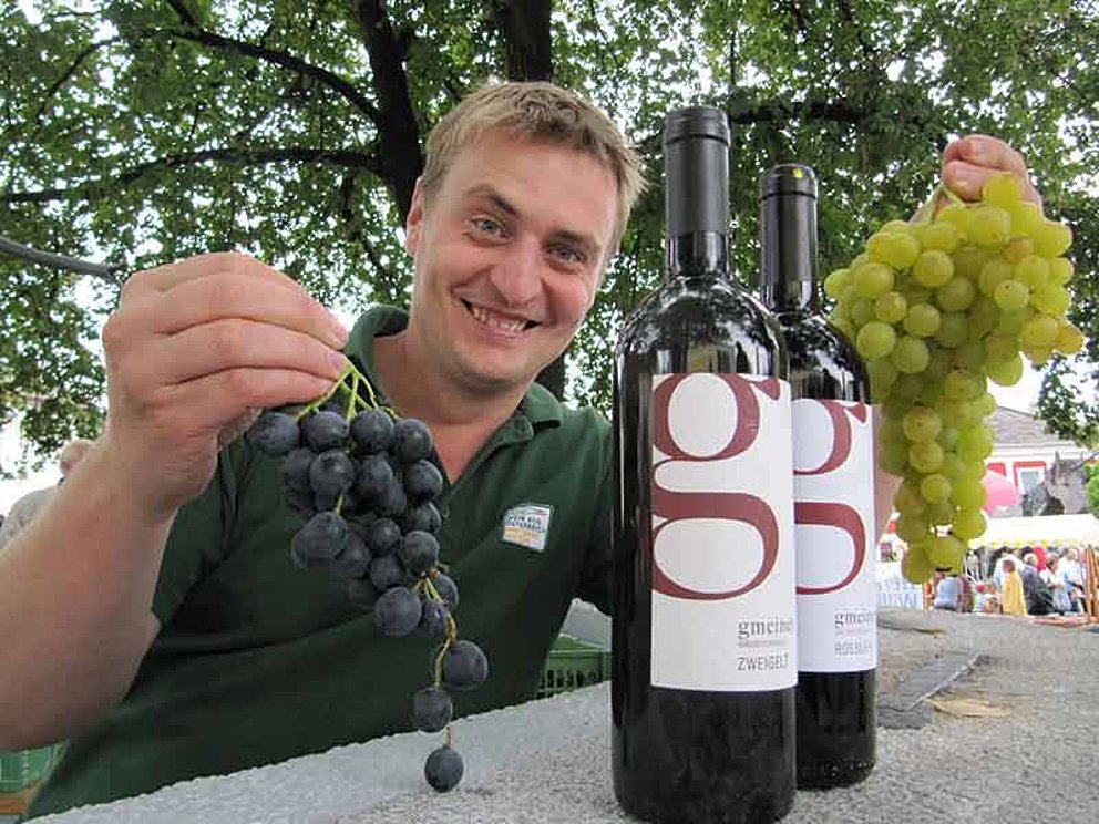 Weinbauer Gmeiner mit Weinflaschen und rot und weißer Weinreben