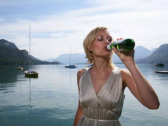 Ein Frau trinkt aus einer Bierflasche am Seeufer