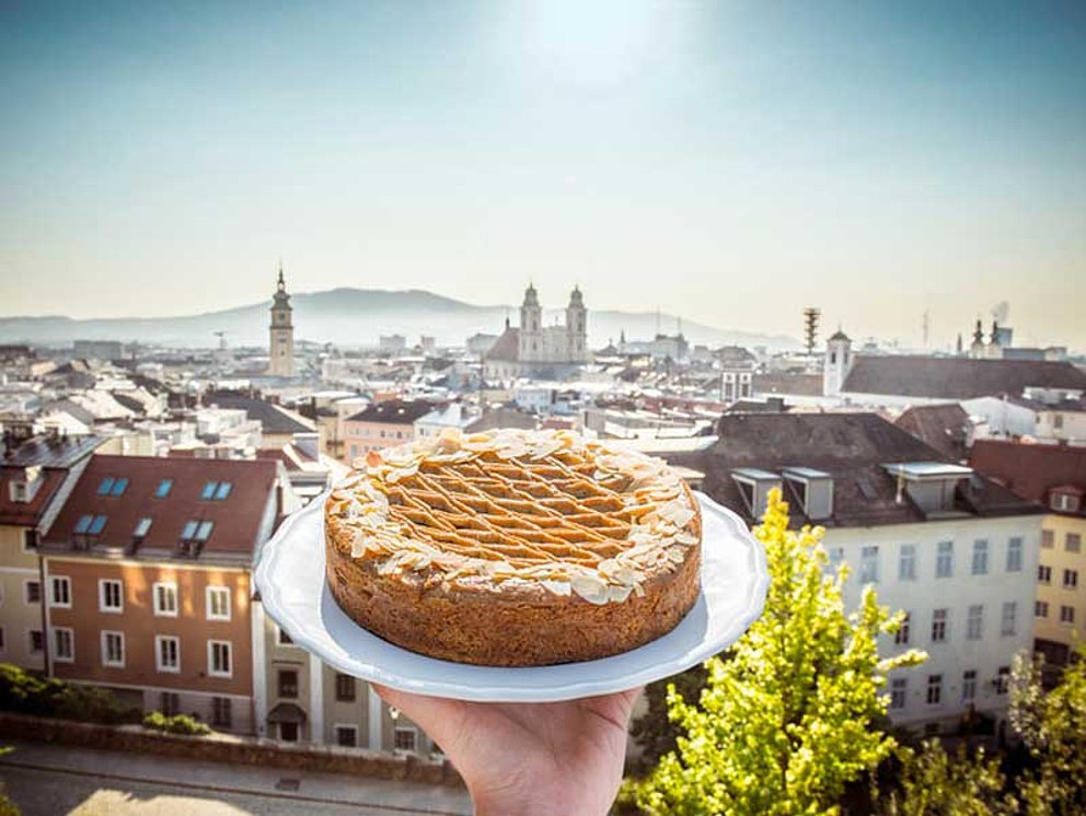Linz Torte auf einem Servierteller getragen, im Hintergrund die Stadt Linz