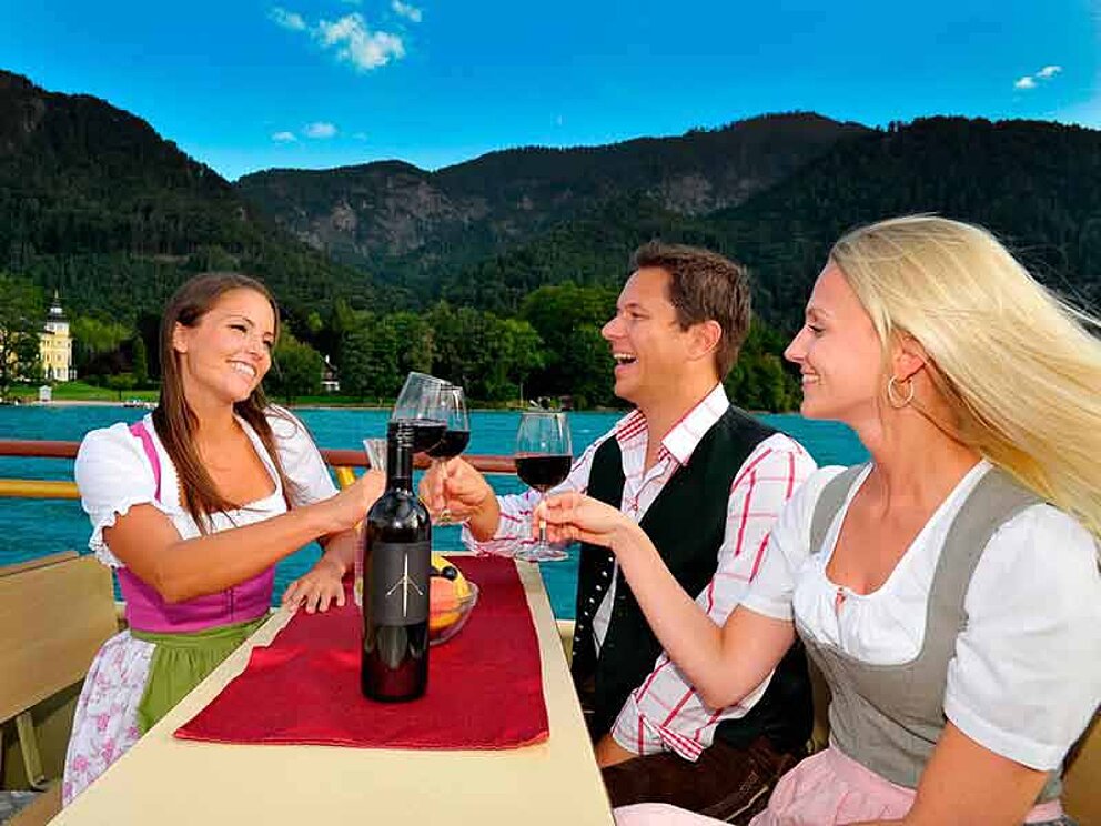 zwei Frauen und ein Mann beim Anstoßen mit Wein bei einer Schifffahrt am Attersee im Salzkammergut