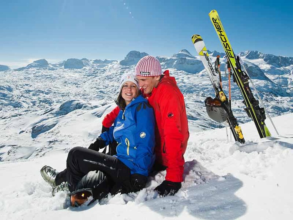 Paar sitzt im Schnee und genießt die Wintersonne 