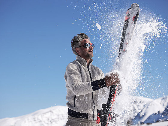 ein Mann klopf sein Skier zusammen, eine Schneewolke entsteht.