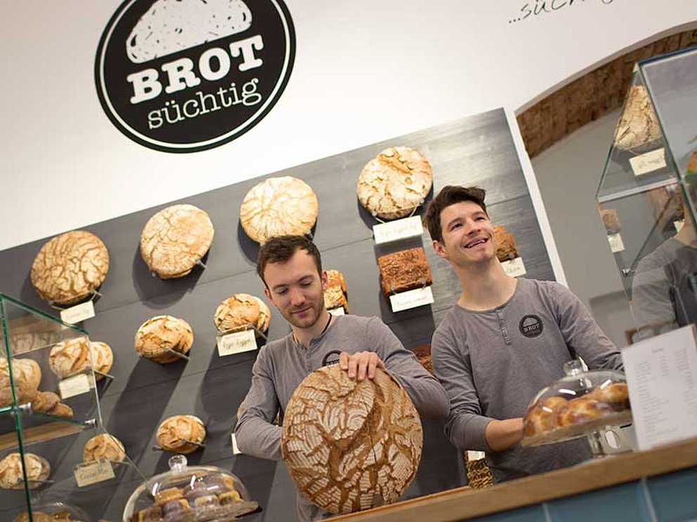Die Bäcker Stefan und Oliver im Verkaufsraum umgeben von vielen Laiben Brot