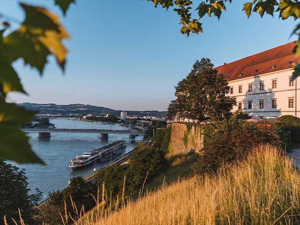 rechts das Linzer Schloss, am Fuße des Schlossberges die Donau mit einem Kreuzfahrtschiff.