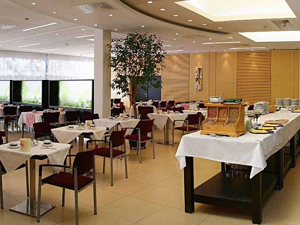 Speisesaal im Hotel Sommerhaus in Linz. Im Saal befinden sich Einzeltische und Stühle. Rechts ist ein Buffet mit Rechauds aufgebaut.