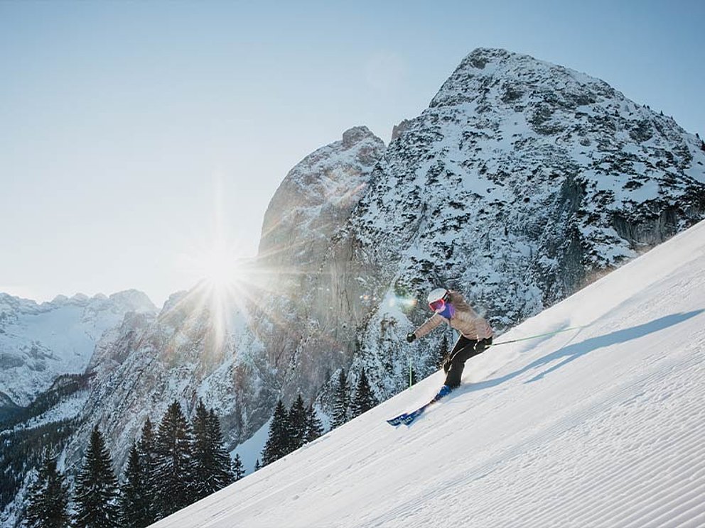 Eine Skifahrerin auf einer leeren Piste, im Hintergrund Bergpanorama