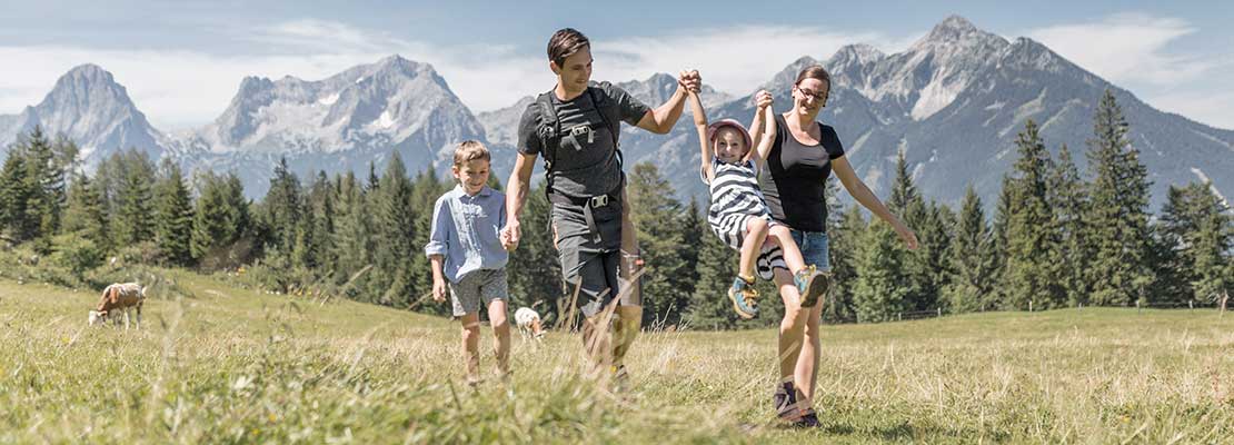 Familie wandert über eine Sommerwiese, im Hintergrund Berggipfel
