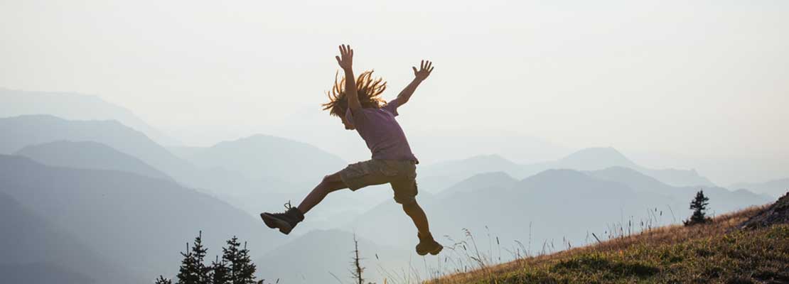 Kind springt mit ausgestreckten Armen und Beinen über eine Bergwiese