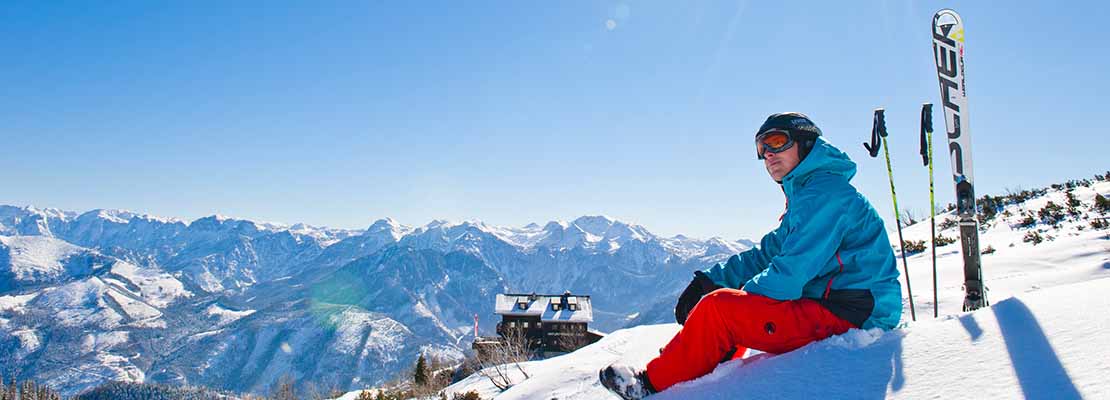 Skifahrer sitzt auf Piste mit tollem Panorama des Feuerkogels