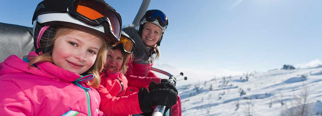 2 Mädchen mit Mama am Sessellift im Skigebiet